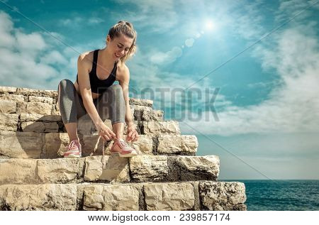 Women runner bootlace on her boot after running in sunny day under sunlight from blue sky near the sea.