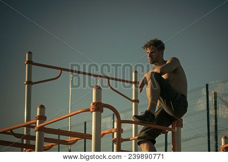 Climb, Climbing Frame. Man Sit On Metal Jungle Gym On Blue Sky. Sport, Health, Recreation. Sportsman