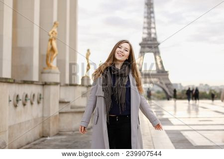 Cheerful Female Peson In Grey Coat Standing On Trocadero Square Near Gilded Statues And Eiffel Tower
