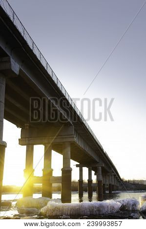 Road Bridge Over The River, On The Banks Of Which Lies The Ice At Sunsetroad Bridge Over The River A