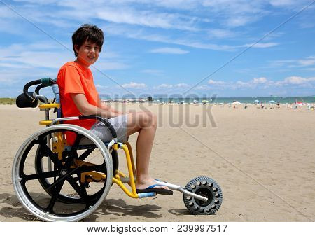 Young Boy With Disabilities On Wheelchair In The Beach Near The Sea In Summer