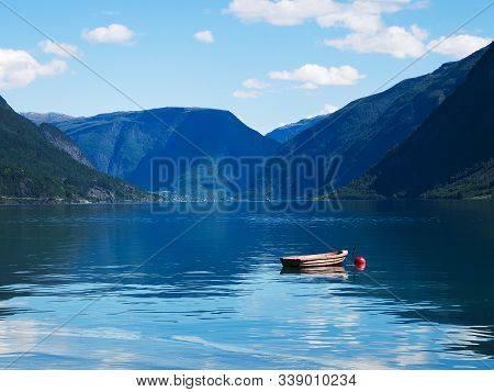 Small Wooden Boat Moored To A Red Buoy Floats On Waters Of The Lustrafjord In Norway, With Reflectio