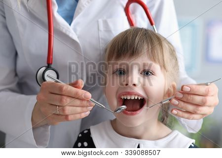 Portrait Of Joyful Little Girl Visiting Dentist And Looking At Camera With Joyfulness. Doctor In Whi