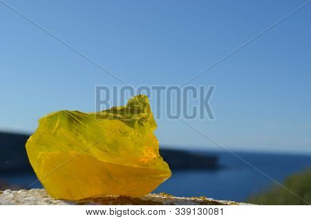 Piece Of Yellow Glass On A Wall, With The Horizon As Background. Blue Sky And Cliff.