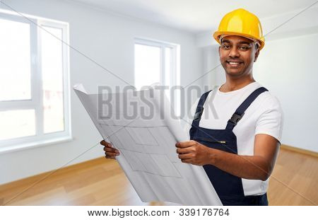 profession, construction and building concept - happy smiling indian builder or repairman in helmet with blueprint over empty room background
