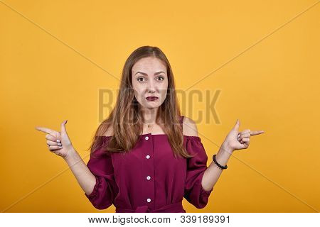 Girl In Burgundy Bluse Over Isolated Orange Background Undecided Pointing Fingers In Different Direc