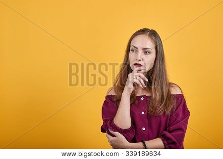 Ginger Girl In Burgundy Bluse With Bow Over Isolated Orange Background Thoughtfully Looks Left And H