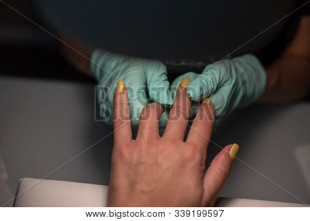 A Manicure Hand With A Nail Lies On A Manicure Hand In Blue Hygienic Gloves.hands On The Manicure Of