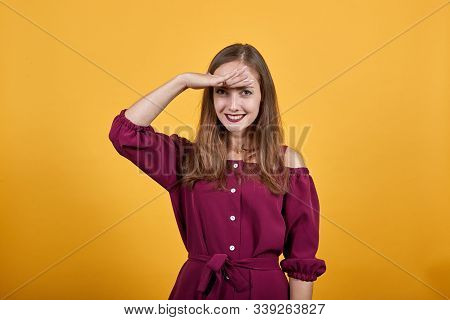 Young Lady In Burgundy Bluse With Bow Over Isolated Orange Background Looking Far Away With Hand To 