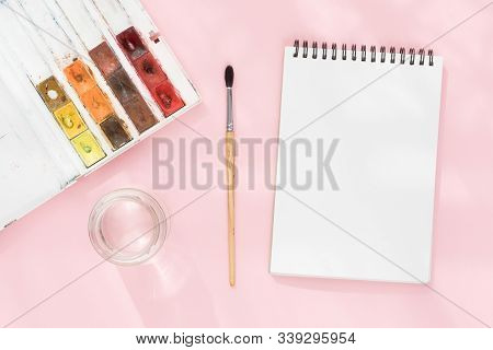 White Clean Notepad On Black Spring, Squirrel Brush, Jar Of Water And Watercolor Paints On Pink Pape