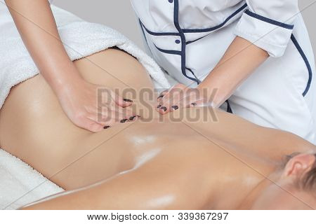 Masseur Makes A Relaxing Massage On The Lower Back And  Back Of A Young Beautiful Woman In A Spa. Co