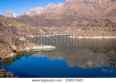 Reflection Of Mountains In The Clear Bright Blue Water Of The Lake. Snowy Peaks Are Visible In The D