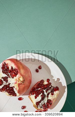 Sliced Pomegranate On A White Plate On A Green Background Close-up