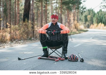 Training An Athlete On The Roller Skaters. Biathlon Ride On The Roller Skis With Ski Poles, In The H
