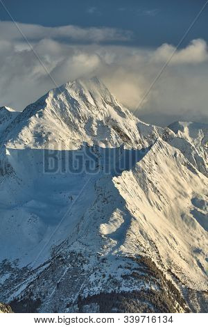 Snowy high mountains scenic landscape with clouds around the rocky peak