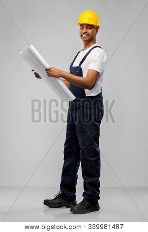 profession, construction and building - happy smiling indian builder in helmet with blueprint over grey background