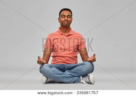 meditation, mindfulness and people concept - happy indian mant meditating in lotus yoga pose over gray background