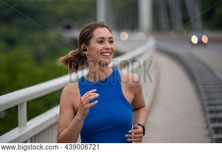 Active Woman Smiling Exerising Outdoors. Young Athlete Listening To Music Running Jogging On Bridge.