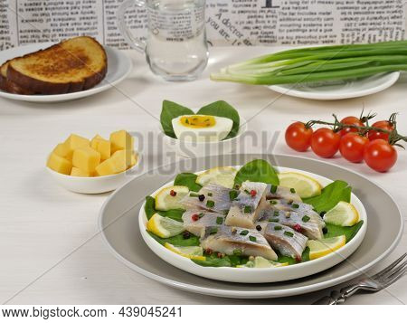 Herring Fish With Lemon On Spinach Leaves On A White Plate, Cherry Tomatoes, Cheese, Egg, Green Onio