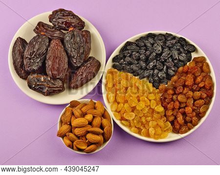 Dried Fruits. Dried Dates, Light, Brown, Dark Raisins On A Round White Plate, Almonds In A Cup On A 