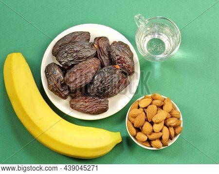 Dried Dates On A Plate, Almonds, Banana And A Glass Of Water On An Emerald Background. Close-up. Top