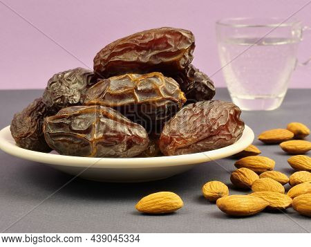 Dried Dates On A Plate, Almonds And A Glass Of Water On The Table On A Lilac Background. Ramadan . C