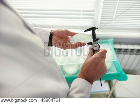 Close-up Of Hands Of Plastic Surgeon Holding A Silicone Breast Implant And Measuring Its Size With A