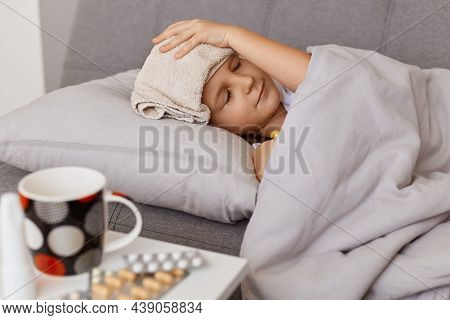 Side View Of Sick Unhealthy Little Baby Girl With Fever, Having Wet Towel On Her Forehead To Lower T