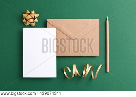 Empty Card, Kraft Envelope, Wooden Pencil And Golden Decorations On Green Background. Holiday And In