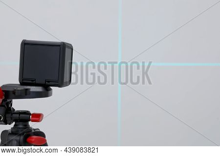 Cross Line Laser Level On Tripod In Front Of Grey Wall