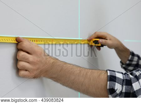 Man Using Cross Line Laser Level And Tape For Accurate Measurement On Light Wall, Closeup