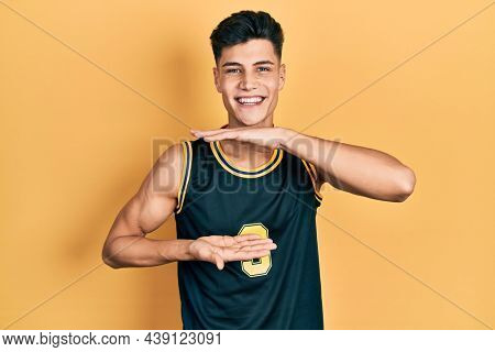 Young hispanic man wearing basketball uniform gesturing with hands showing big and large size sign, measure symbol. smiling looking at the camera. measuring concept. 