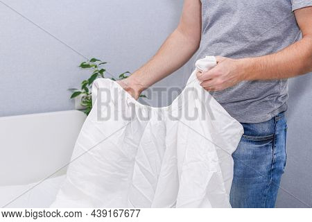A Man Puts An Elasticated Sheet On The Mattress. Change Of Bed Linen.