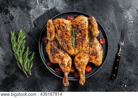 Tobacco Whole Chicken On Plate With Herbs And Tomato. Black Background. Top View
