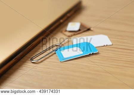 Sim Cards, Mobile Phone And Ejector Tool On Wooden Table, Closeup
