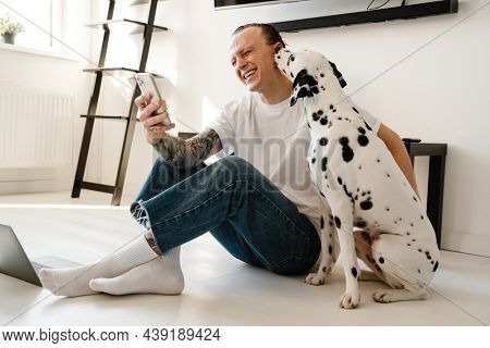 Young happym mid aged man with laptop computer taking a selfie while sitting on a floor with his dog at home