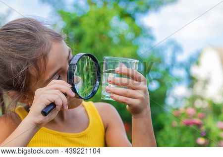 The Child Examines A Glass Of Water With A Magnifying Glass. Selective Focus.