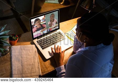 African american woman using laptop for video call, with diverse elementary school pupils on screen. communication technology and online education, digital composite image.