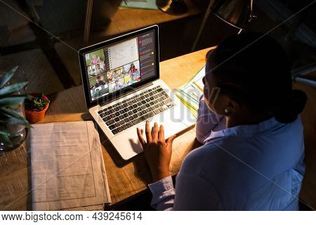 African american woman using laptop for video call, with diverse elementary school pupils on screen. communication technology and online education, digital composite image.
