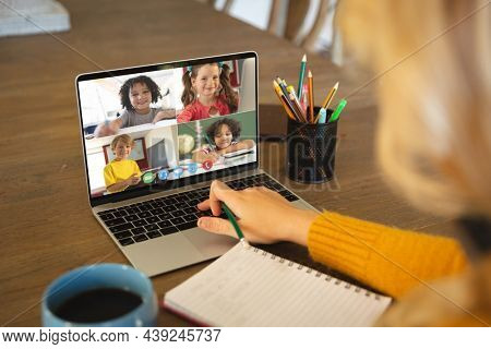 Caucasian woman using laptop for video call, with smiling diverse elementary school pupils on screen. communication technology and online education, digital composite image.