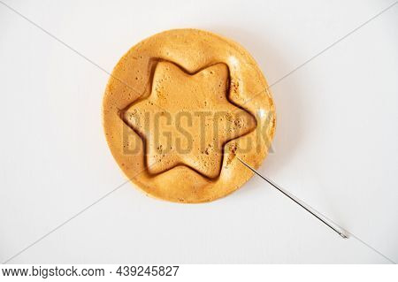 Brown sugar caramel candy cookies with a metal needle in the shape of a star on a white background.