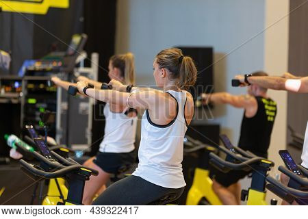 Rimini, Italy - September  2021: Girl Having Workout At Gym With Indoor Exercise Bike And Small Dumb