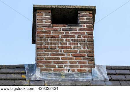 An Isolated Portrait Of A Small Masonry Grout Red Brick Chimney On A Black Tile Roof On An Overvast 