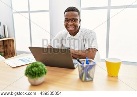 Young african man working at the office using computer laptop happy face smiling with crossed arms looking at the camera. positive person. 