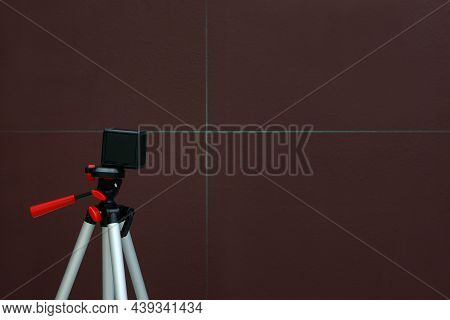 Cross Line Laser Level On Tripod In Front Of Brown Wall