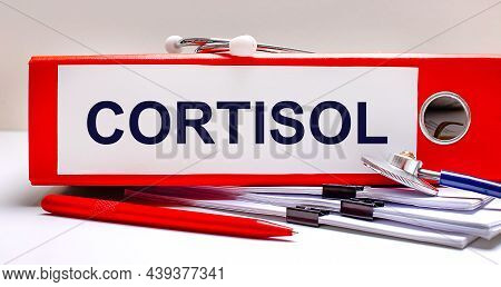 On The Desktop Is A Stethoscope, Documents, A Pen, And A Red File Folder With The Text Cortisol. Med