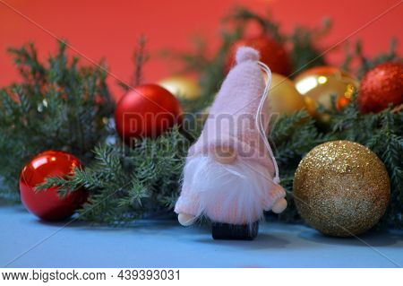 A Gnome In A Pink Outfit Stands Next To A Spruce Branch