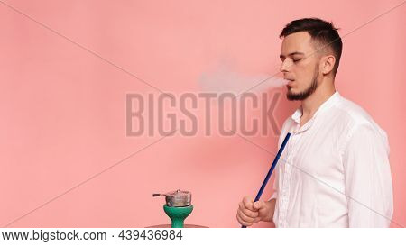 A Male Model Smokes A Hookah, Sheesha And Enjoys It. Pink Background