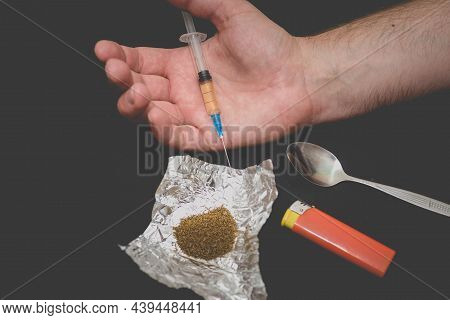 Drug Addict Hand With Syringe On Dark Room With A Bag Of Drugs A Spoon And A Lighter.toned.