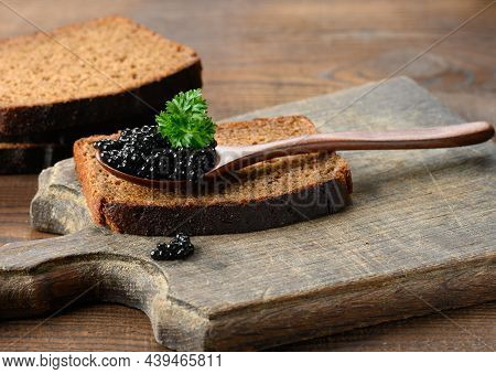 Fresh Grainy Black Paddlefish Caviar In Brown Wooden Spoon On A Brown Table, Close Up